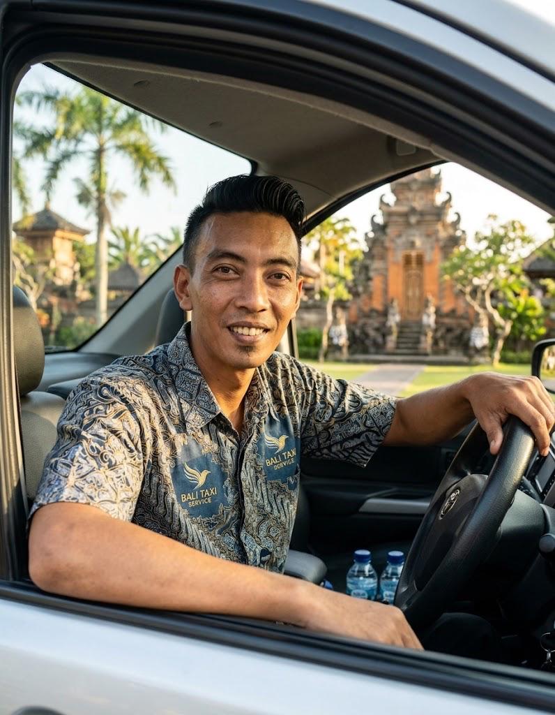 Gede Jedot at the wheel of his car, smiling, with a Balinese temple gate behind him